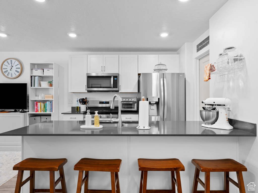 Kitchen featuring a breakfast bar, white cabinetry, stainless steel appliances, and kitchen peninsula