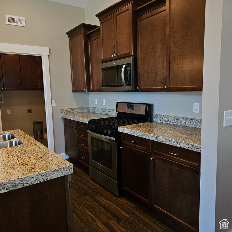 Kitchen with appliances with stainless steel finishes, dark hardwood / wood-style floors, dark brown cabinetry, and light stone countertops