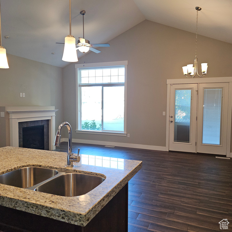 Kitchen with vaulted ceiling, dark wood-type flooring, a tile fireplace, pendant lighting, and sink