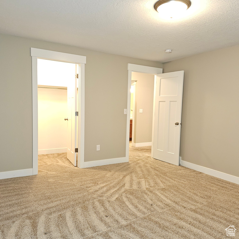 Unfurnished bedroom with light carpet, a walk in closet, a textured ceiling, and a closet