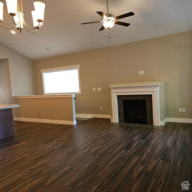 Unfurnished living room with lofted ceiling, a tiled fireplace, dark hardwood / wood-style floors, and ceiling fan with notable chandelier