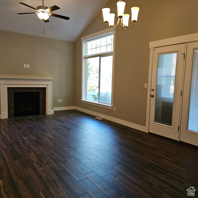 Unfurnished living room with lofted ceiling, ceiling fan with notable chandelier, a tile fireplace, and dark hardwood / wood-style flooring