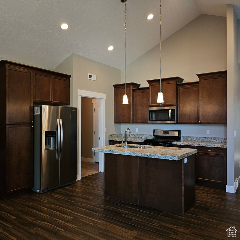 Kitchen featuring hanging light fixtures, an island with sink, appliances with stainless steel finishes, high vaulted ceiling, and dark wood-type flooring