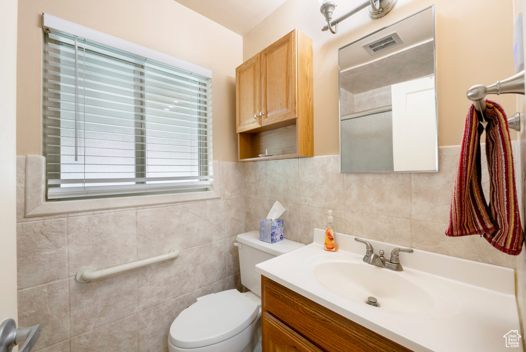 Bathroom featuring vanity, toilet, tile walls, and a shower