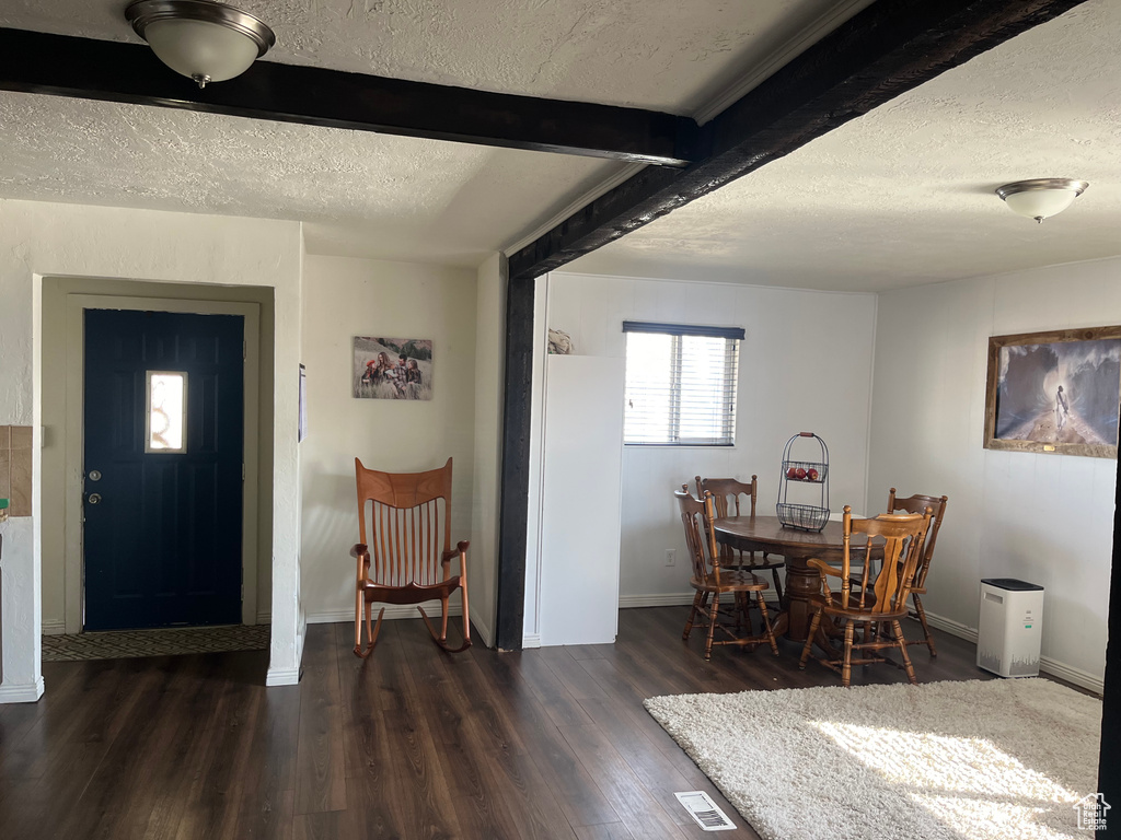 Dining room with a textured ceiling, dark hardwood / wood-style floors, and beam ceiling