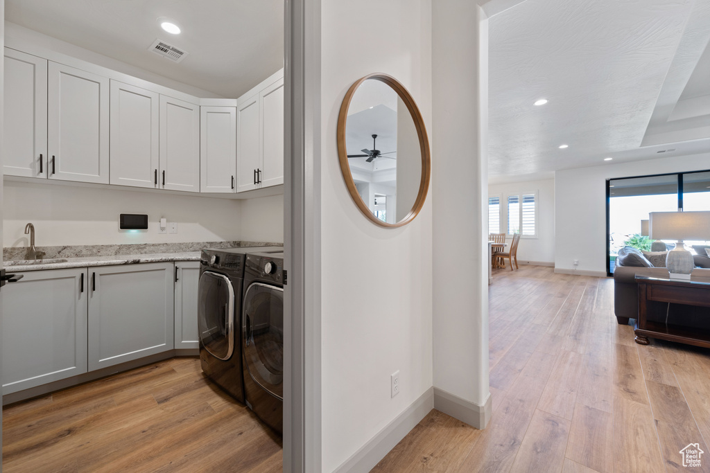 Washroom featuring sink, washing machine and clothes dryer, light hardwood / wood-style floors, ceiling fan, and cabinets