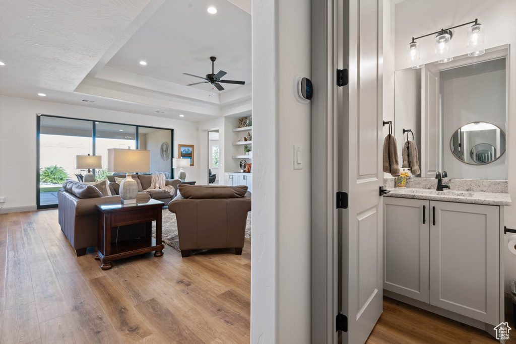 Living room with light hardwood / wood-style flooring, ceiling fan, sink, and a raised ceiling