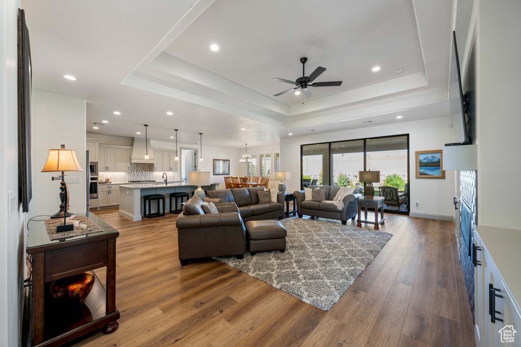 Living room with hardwood / wood-style floors, ceiling fan with notable chandelier, and a raised ceiling