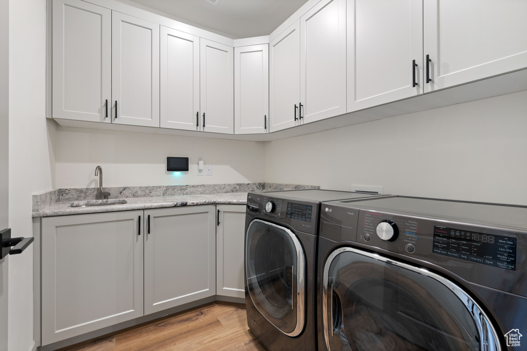 Laundry room featuring sink, washer and dryer, light wood-type flooring, and cabinets