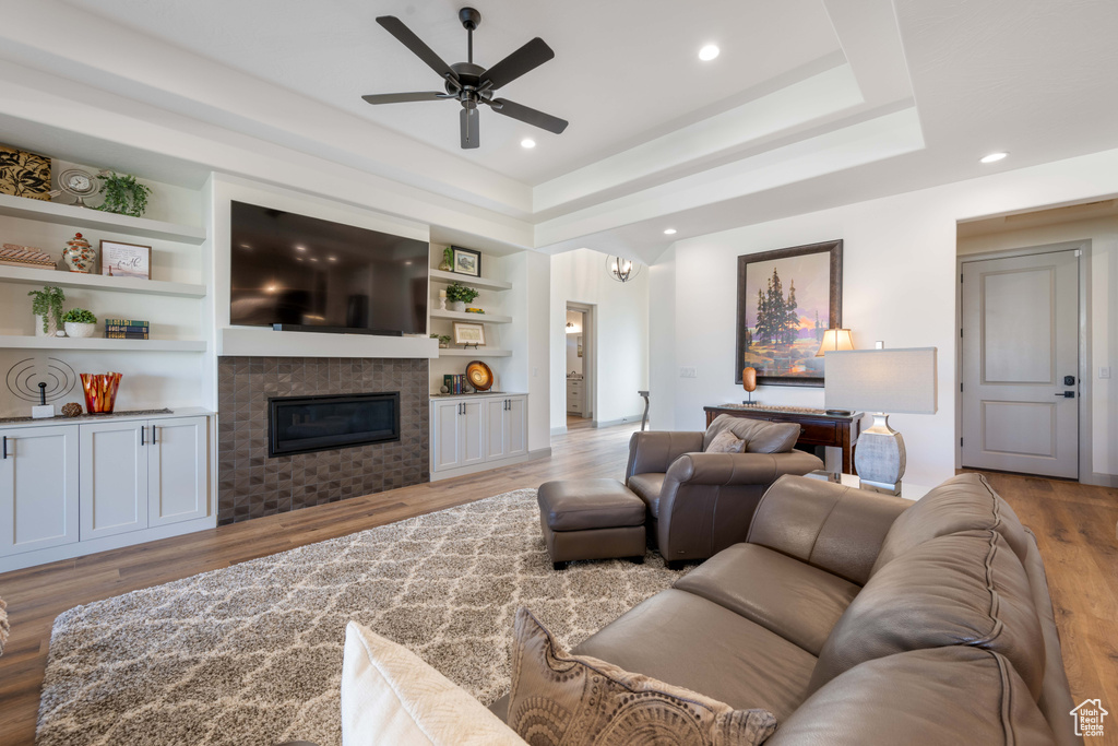 Living room featuring light hardwood / wood-style flooring, ceiling fan, a tray ceiling, and built in shelves