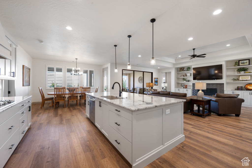 Kitchen with dark wood-type flooring, an island with sink, sink, light stone countertops, and white cabinetry