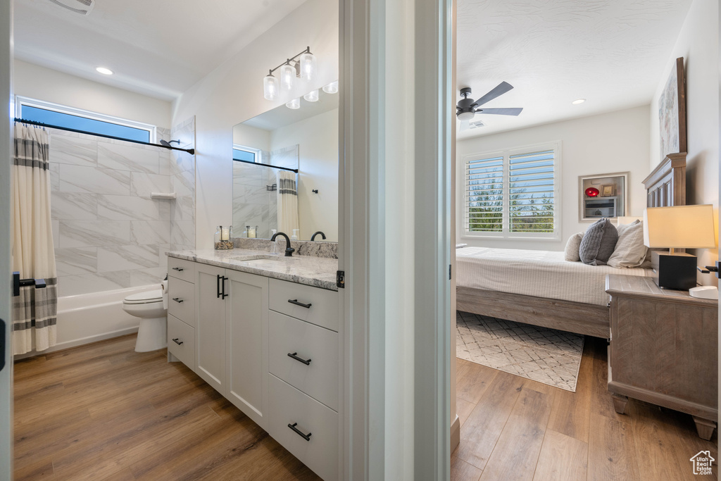 Full bathroom with hardwood / wood-style floors, shower / bath combination with curtain, toilet, ceiling fan, and vanity