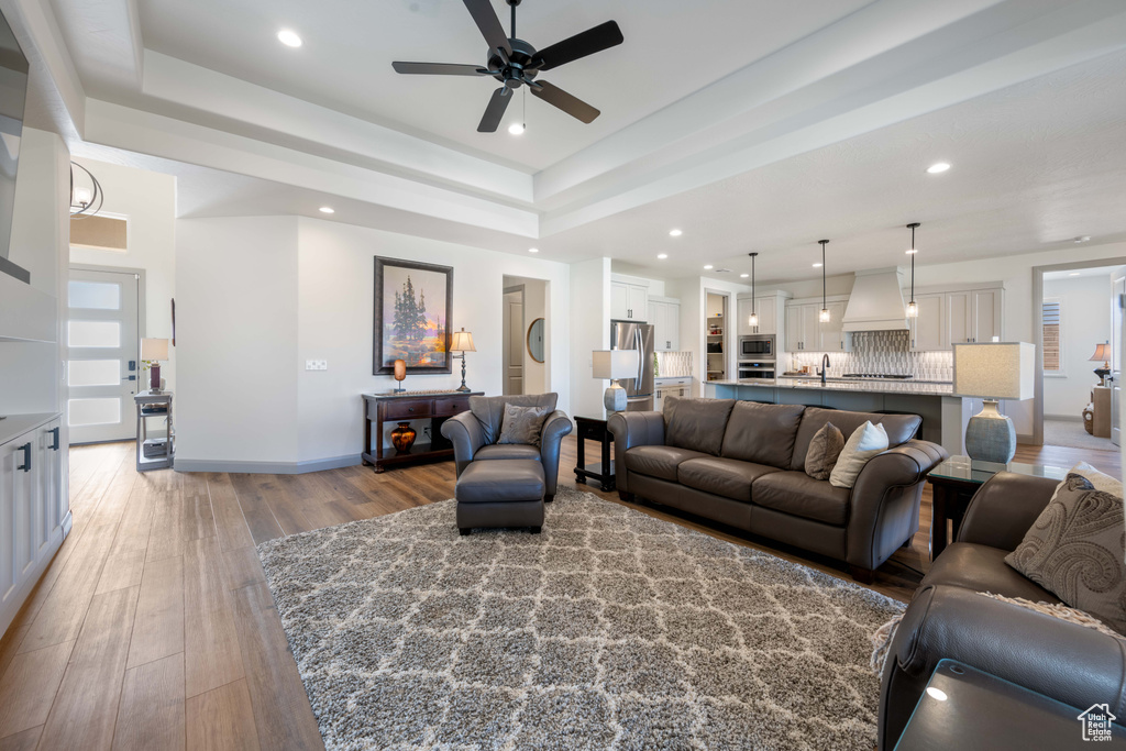 Living room featuring sink, a tray ceiling, light wood-type flooring, and ceiling fan