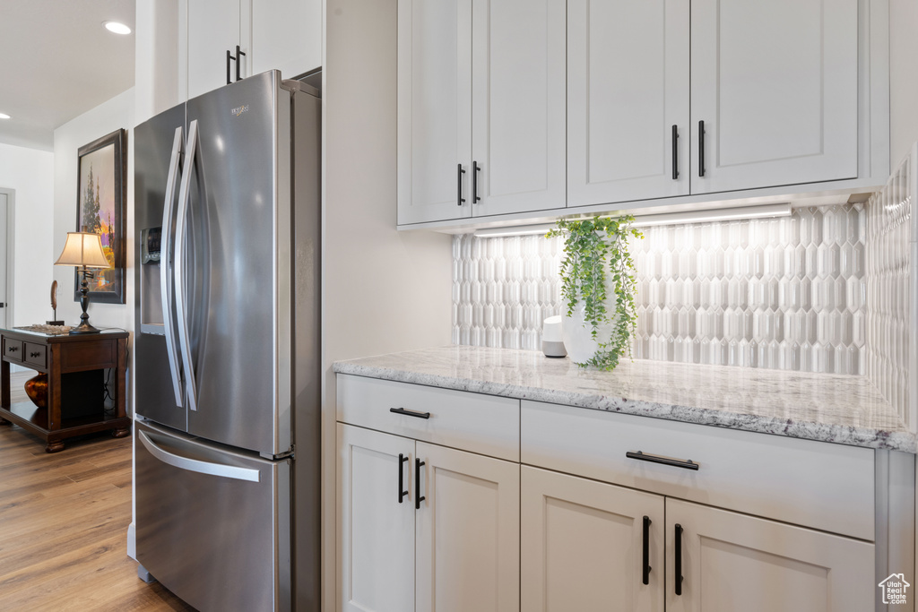 Kitchen featuring light hardwood / wood-style flooring, stainless steel refrigerator with ice dispenser, backsplash, white cabinetry, and light stone counters