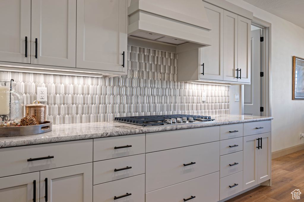 Kitchen featuring decorative backsplash, premium range hood, white cabinetry, stainless steel gas cooktop, and light hardwood / wood-style floors