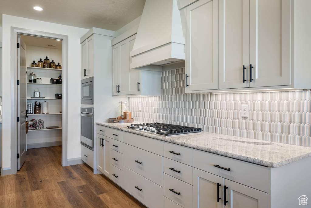 Kitchen featuring light stone countertops, appliances with stainless steel finishes, white cabinetry, custom exhaust hood, and dark hardwood / wood-style floors