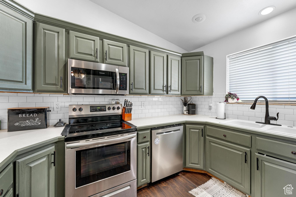 Kitchen with backsplash, vaulted ceiling, stainless steel appliances, sink, and green cabinetry