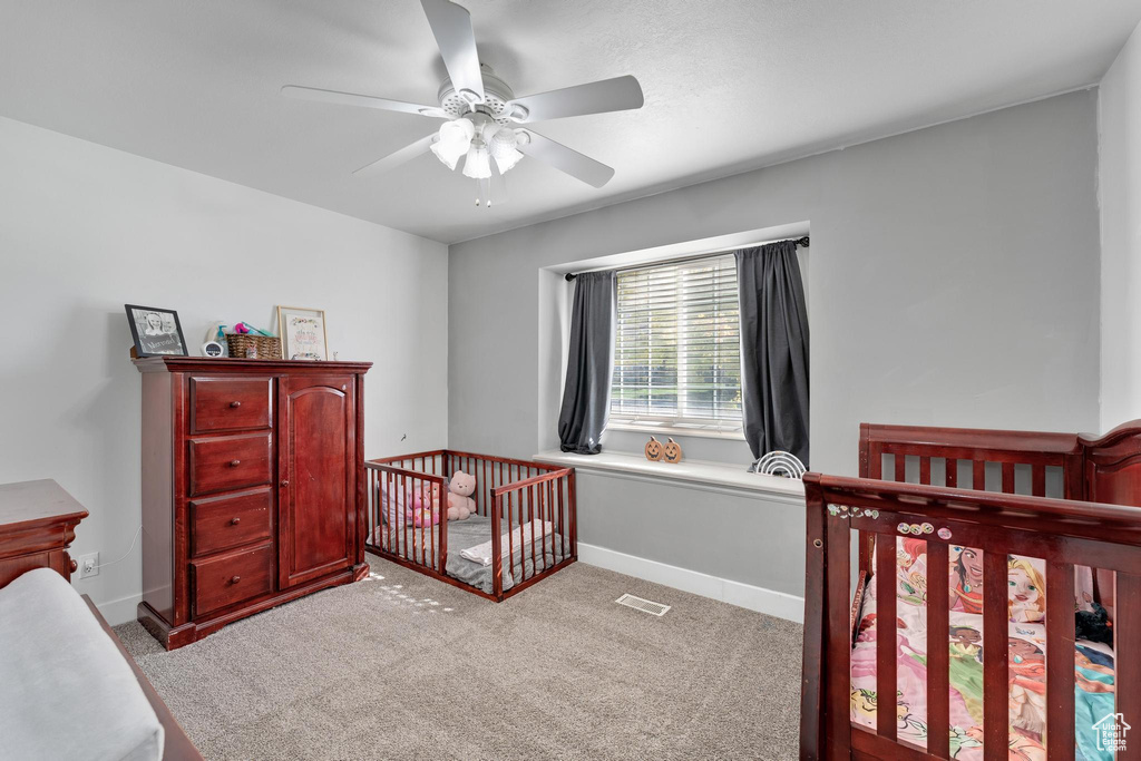 Carpeted bedroom featuring a crib and ceiling fan