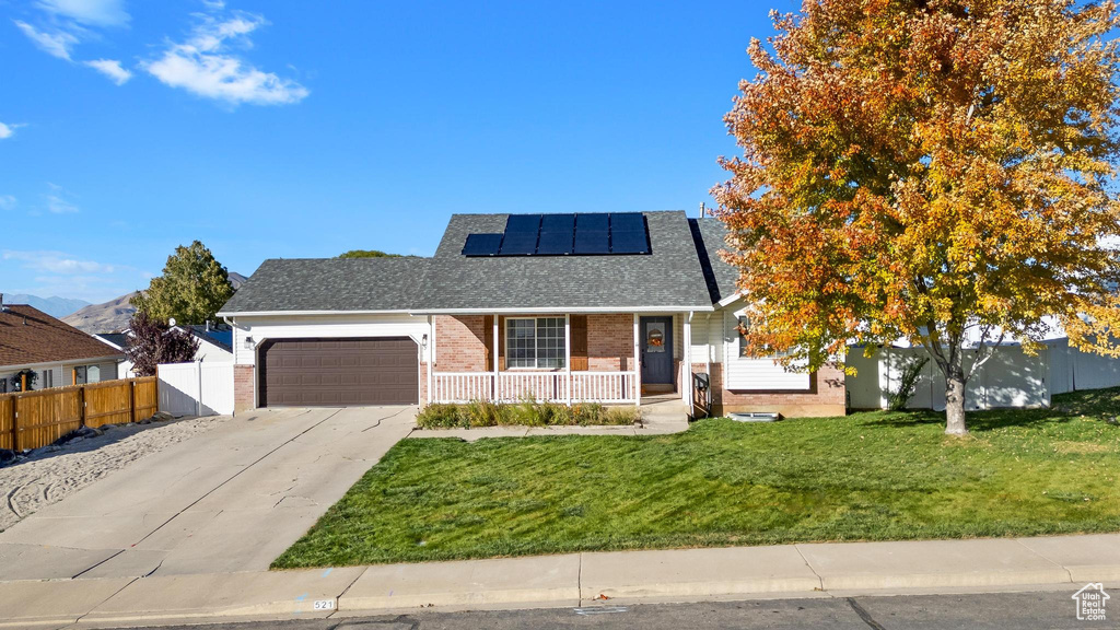 View of front of house featuring a porch, solar panels, a garage, and a front lawn