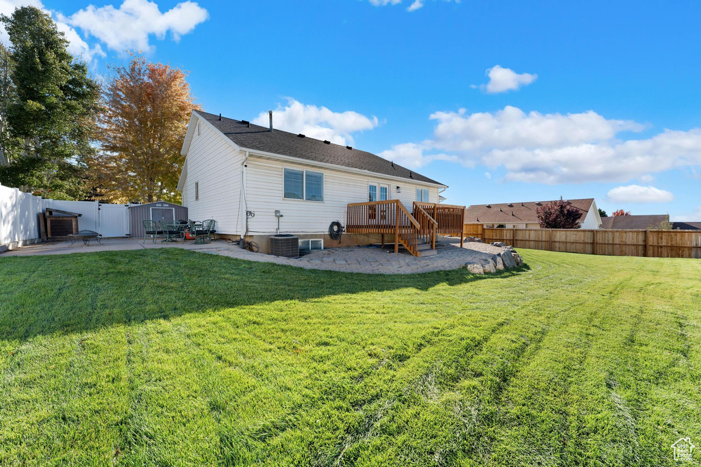 Rear view of house featuring a yard, a wooden deck, and a patio