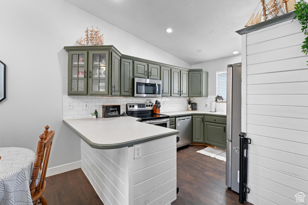 Kitchen featuring appliances with stainless steel finishes, kitchen peninsula, lofted ceiling, dark wood-type flooring, and decorative backsplash