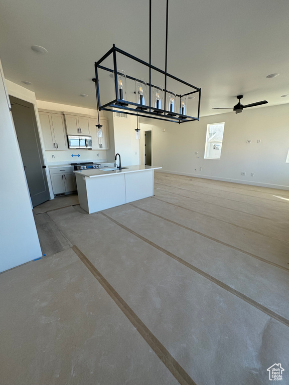 Kitchen with white cabinets, ceiling fan, decorative light fixtures, and an island with sink