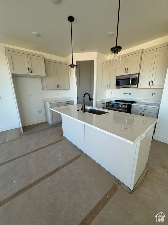 Kitchen with a kitchen island with sink, stainless steel appliances, sink, light stone countertops, and pendant lighting