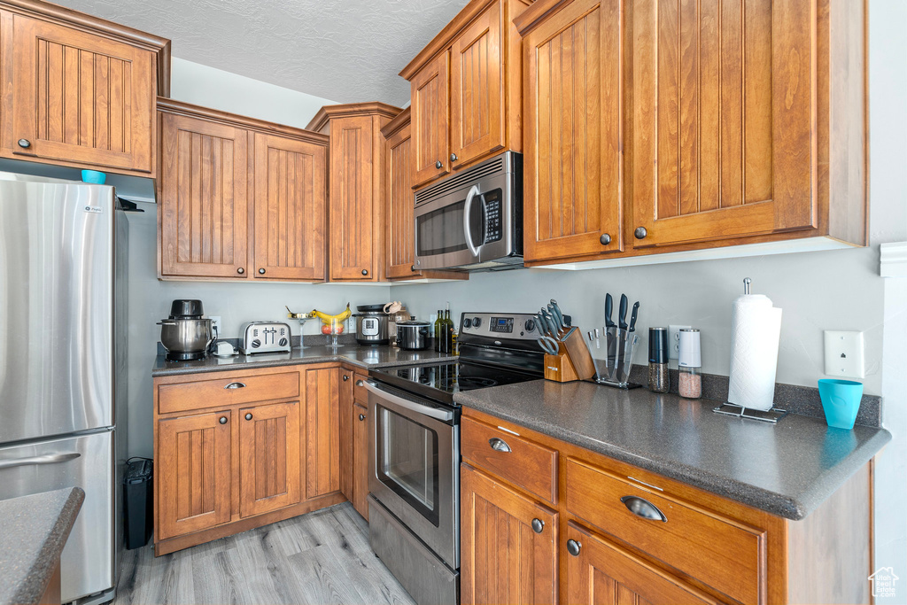 Kitchen featuring appliances with stainless steel finishes, light hardwood / wood-style flooring, and a textured ceiling