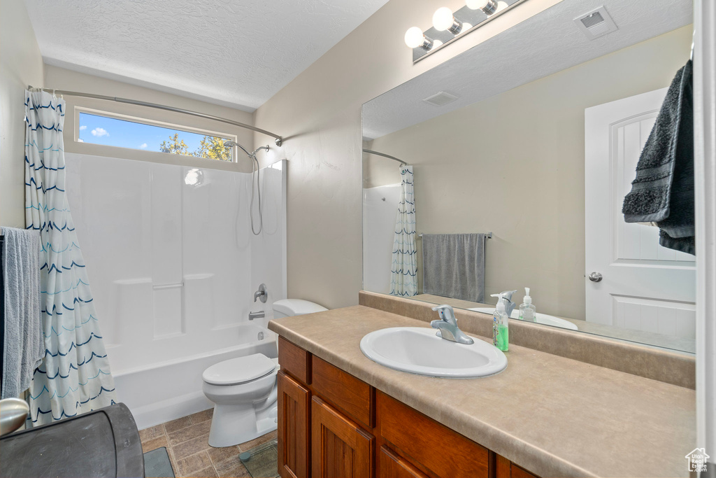 Full bathroom featuring vanity, a textured ceiling, toilet, and shower / bathtub combination with curtain