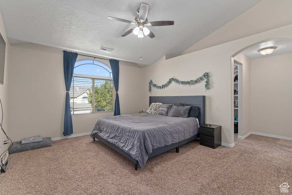 Carpeted bedroom with ceiling fan, a textured ceiling, and lofted ceiling