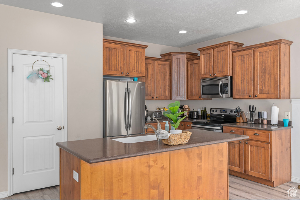 Kitchen with appliances with stainless steel finishes, sink, light wood-type flooring, an island with sink, and a textured ceiling