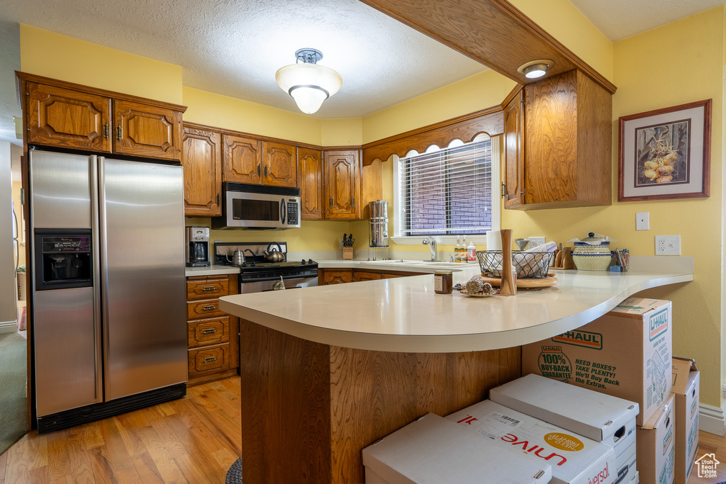 Kitchen featuring kitchen peninsula, a breakfast bar area, a textured ceiling, light wood-type flooring, and stainless steel appliances