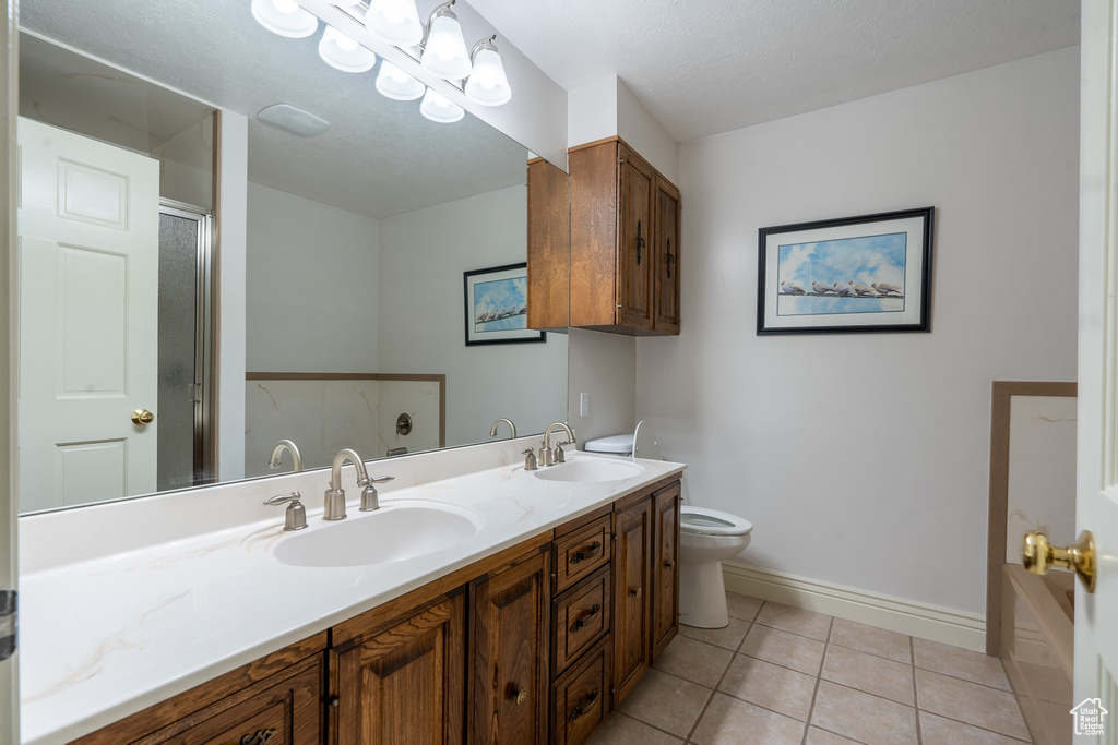 Bathroom with a textured ceiling, a shower with shower door, toilet, tile patterned floors, and vanity