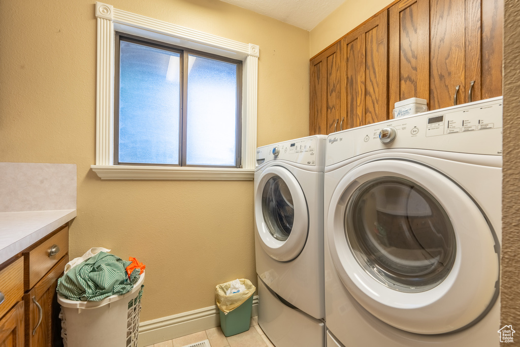 Washroom with light tile patterned flooring, cabinets, and washing machine and clothes dryer
