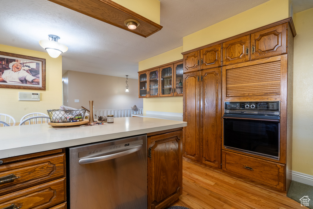 Kitchen featuring stainless steel dishwasher, light hardwood / wood-style floors, hanging light fixtures, and black oven