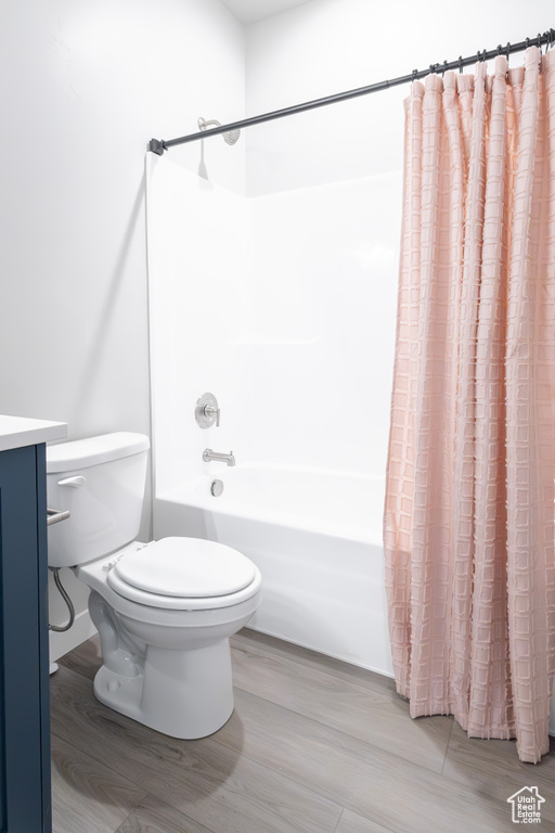 Full bathroom with toilet, shower / tub combo with curtain, hardwood / wood-style flooring, and vanity