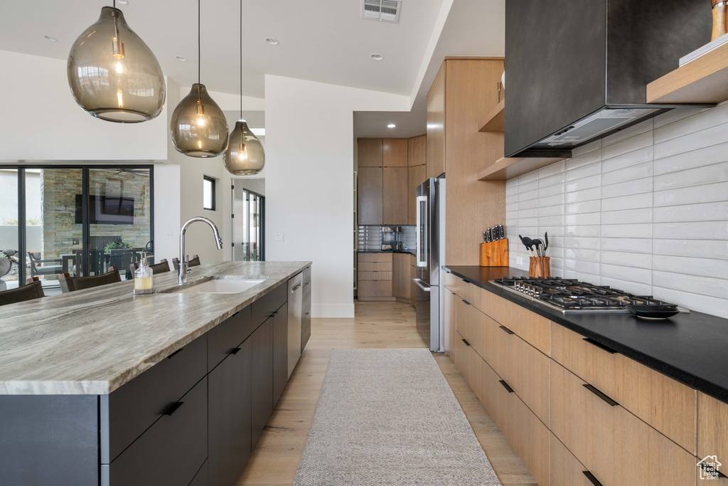 Kitchen featuring a large island with sink, light hardwood / wood-style flooring, backsplash, sink, and decorative light fixtures