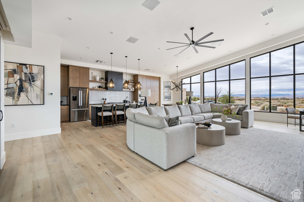 Living room featuring ceiling fan with notable chandelier and light wood-type flooring