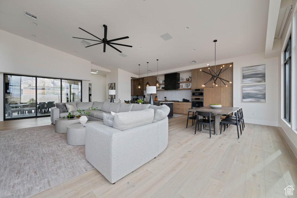 Living room with light hardwood / wood-style floors, high vaulted ceiling, and ceiling fan with notable chandelier