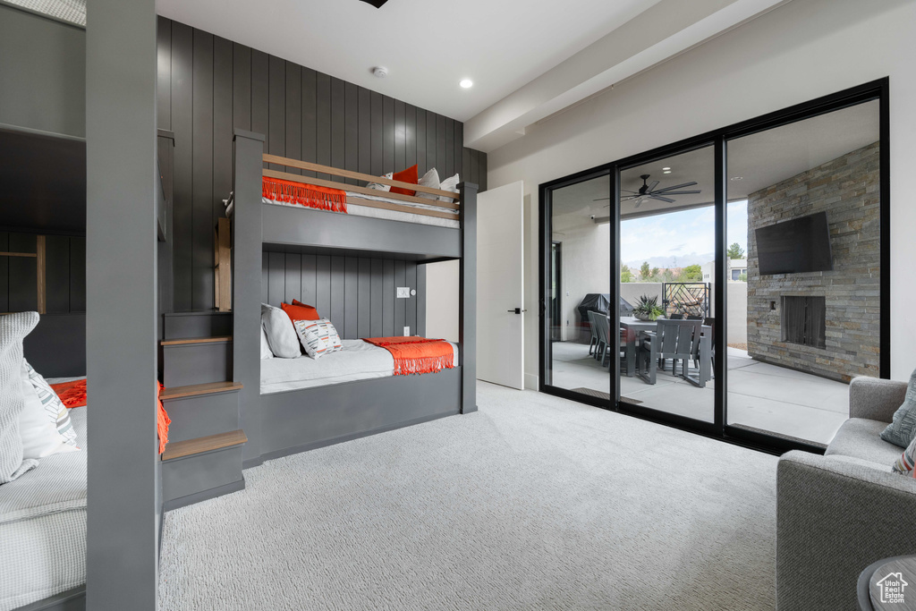 Carpeted bedroom with a stone fireplace, wood walls, and access to exterior