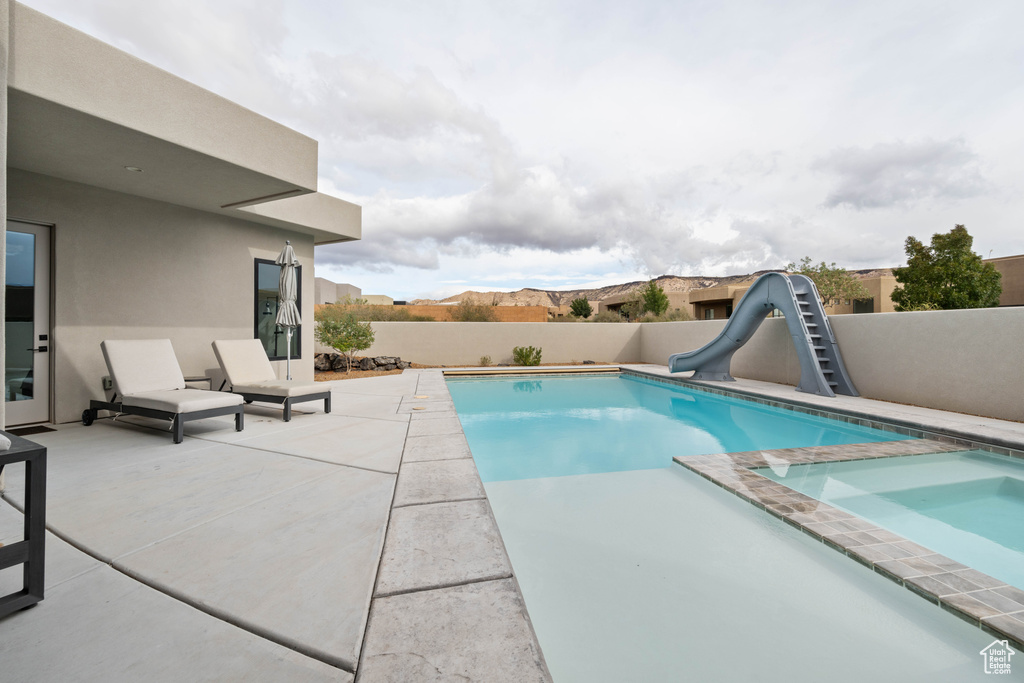 View of pool with an in ground hot tub, a water slide, a mountain view, and a patio area