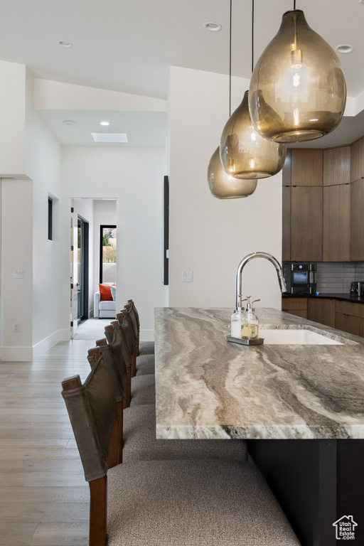 Kitchen featuring dark stone counters, sink, light wood-type flooring, and hanging light fixtures