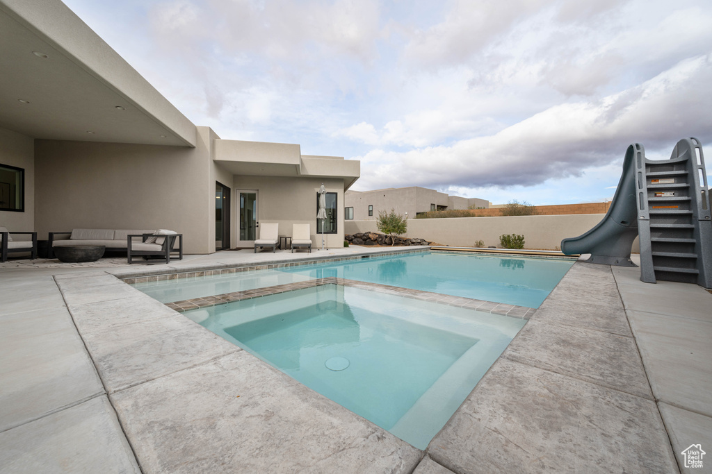 View of pool featuring an in ground hot tub, a patio, a water slide, and an outdoor hangout area