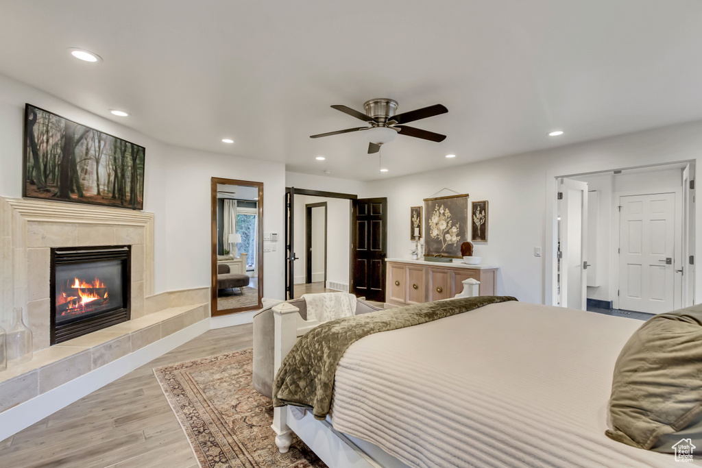 Bedroom featuring a tiled fireplace, light wood-type flooring, and ceiling fan