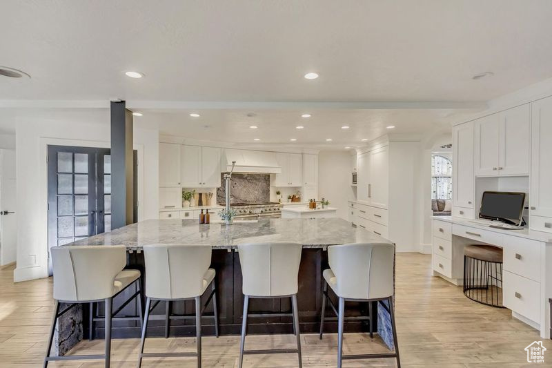 Kitchen featuring decorative backsplash, white cabinets, a large island with sink, light stone countertops, and light wood-type flooring