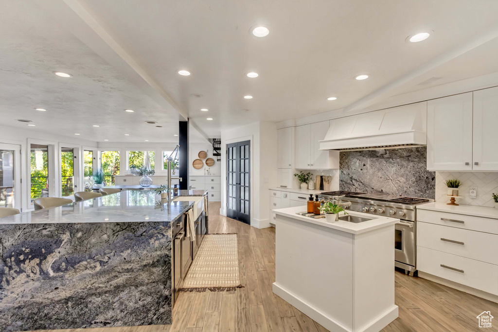 Kitchen featuring high end stainless steel range oven, light wood-type flooring, a spacious island, white cabinetry, and custom range hood