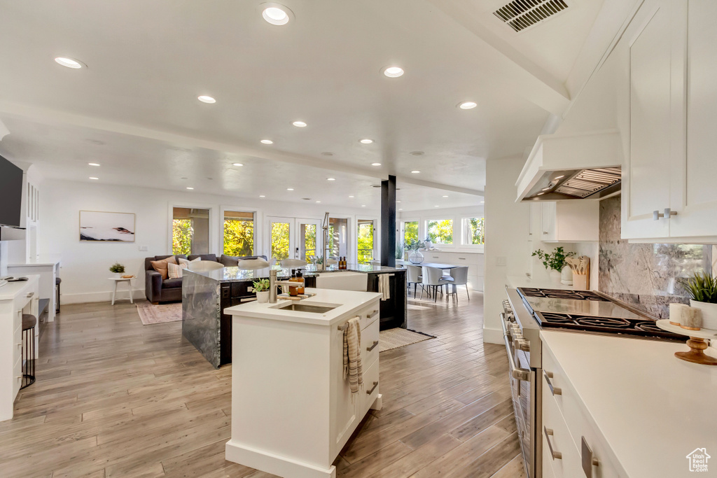 Kitchen featuring an island with sink, white cabinetry, stainless steel stove, and plenty of natural light