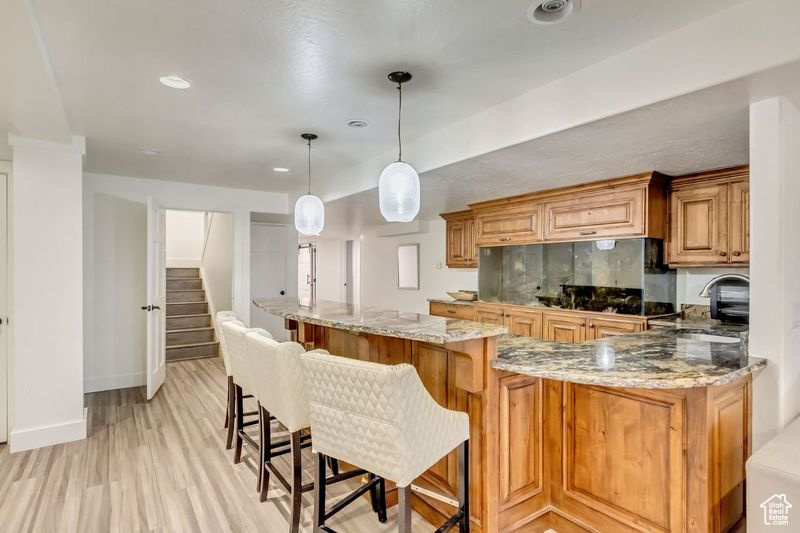 Kitchen with a breakfast bar area, light stone countertops, light wood-type flooring, pendant lighting, and sink