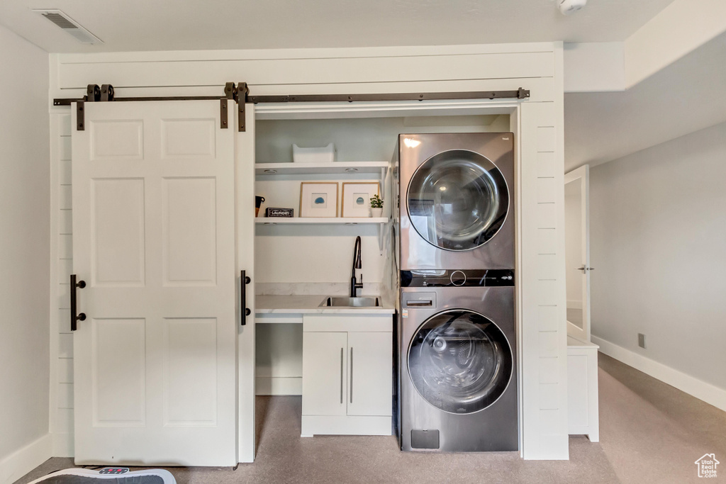 Clothes washing area featuring cabinets, a barn door, stacked washer and clothes dryer, and sink