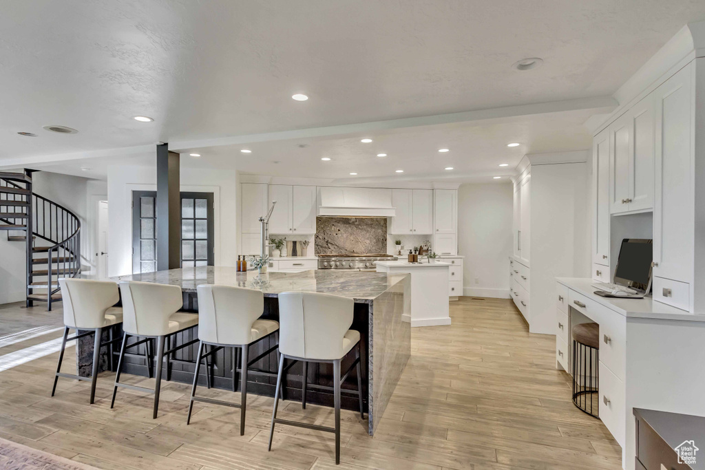 Kitchen with a spacious island, light stone countertops, white cabinetry, and light hardwood / wood-style flooring